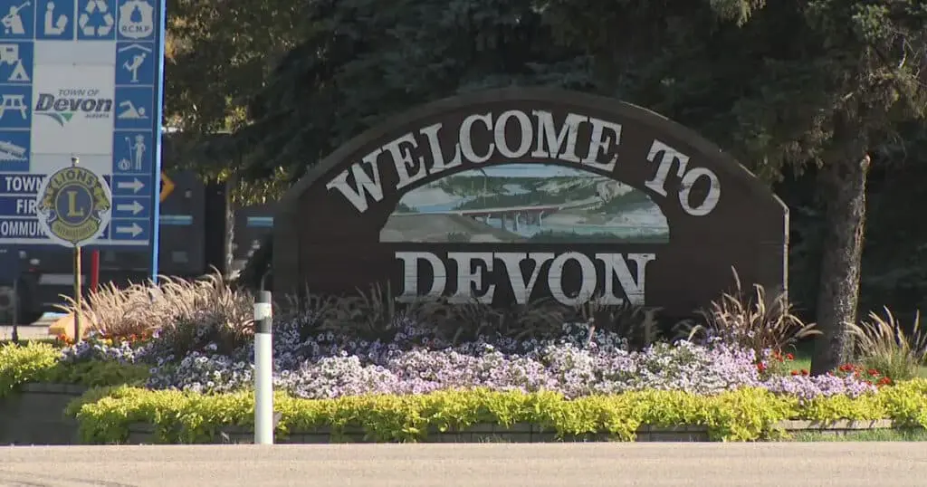 Welcome to Devon sign in Alberta, Canada, featuring lush greenery and colorful flowers.