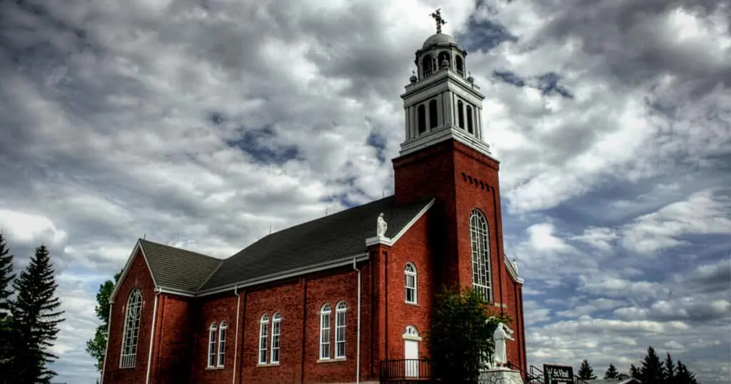 Iconic red brick church in Leduc, Alberta with a tall steeple and classic architecture, set against a dramatic cloudy sky.