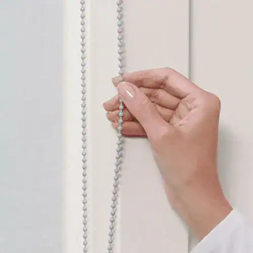 Close-up of a hand adjusting a string of decorative beads, installed on a white door or wall.