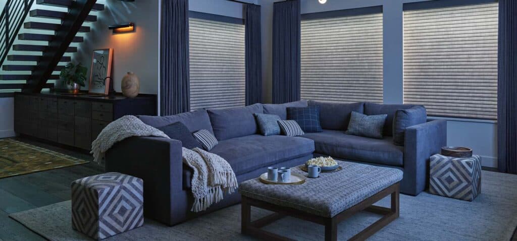 Cozy modern living room with navy sectional sofa, striped pillows, stylish coffee table, decorative stools, and window blinds, creating a comfortable and stylish home atmosphere.