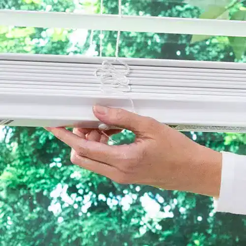 Close-up of a hand adjusting a window blind cord, highlighting safety measures to prevent accidents in homes with children.