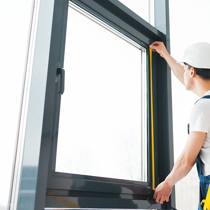 Skilled worker measuring house window frame with tape measure for proper installation and fitting, ensuring quality craftsmanship.