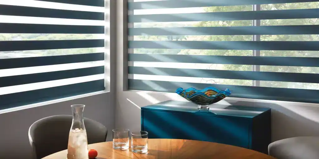 Bright room with layered blue shutters, sunlight filtering in, and a stylish glass bowl on a teal cabinet.