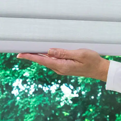 Close-up of a hand gently pulling down window blinds, showcasing easy-to-use window treatment accessories for light control and privacy.
