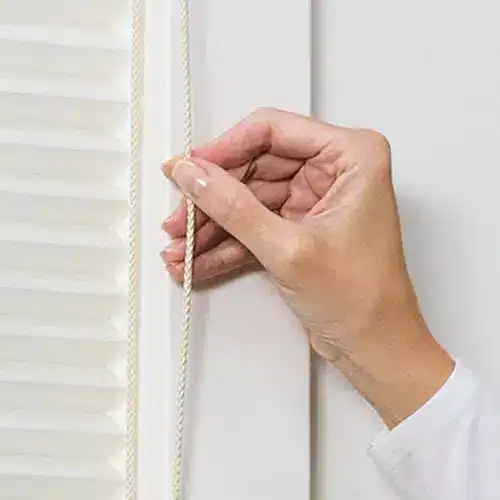 Close-up of a hand adjusting window blinds with a cord, showing interior home decor, window treatments, and window accessories.
