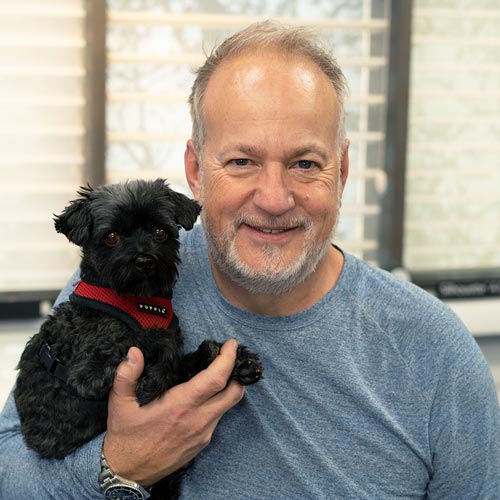 Friendly woman holding small black dog indoors.