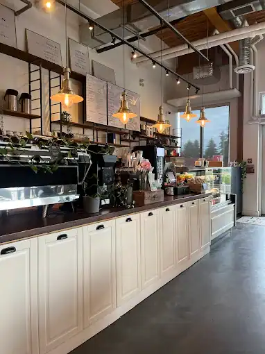 A welcoming coffee shop with a modern, minimalist design featuring a long white counter, warm pendant lighting, and large windows that let in natural light.