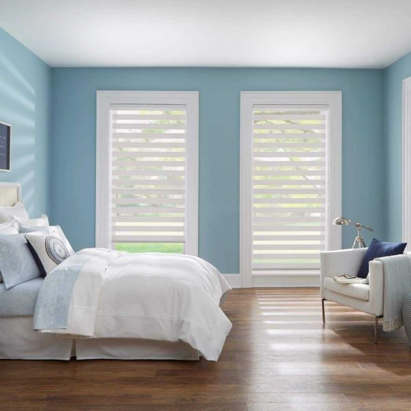 Bright bedroom with light blue walls, white furniture, and large windows with privacy blinds for natural light.